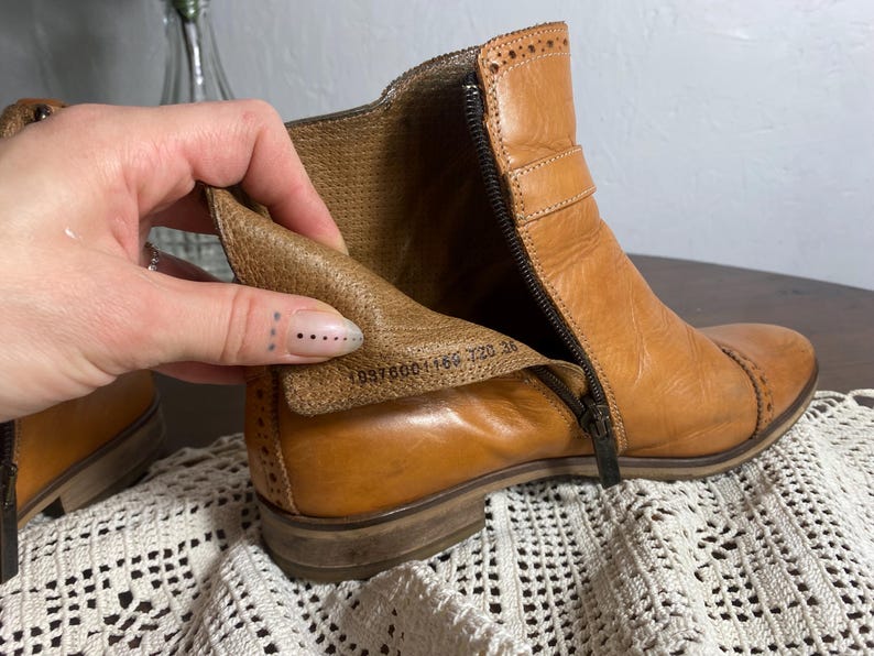 K&ouml;nnte beinhalten: Hellbraune Leder-Ankle Boots mit seitlichem Rei&szlig;verschluss und Ziern&auml;hten. Die Stiefel haben einen niedrigen Absatz und eine Schnalle. Das Innenfutter ist sichtbar. Gr&ouml;&szlig;e 36.