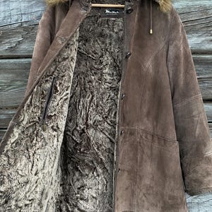 May include: A brown suede coat with a faux fur lining and hood. The coat has a button-up front and a label that reads "Maither". The hood is trimmed with faux fur.