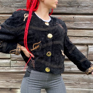 May include: A black suede jacket with gold leaf embroidery and gold buttons. The jacket has a brown and gold patterned lining.