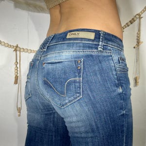 May include: Blue denim jeans with a faded wash. The jeans have a classic five-pocket design, a branded patch, and decorative stitching on the back pockets. The brand name "ONLY" is visible on the patch.