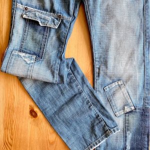 May include: A pair of blue denim jeans with multiple pockets and distressed details. The jeans have a patchwork design with different shades of blue denim.