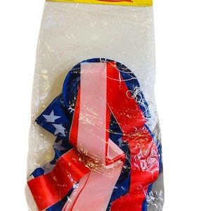 May include: A wind sock in a clear plastic bag. The wind sock is blue with white stars and red and pink ribbons. The top of the bag has a yellow label with the words "WIND SOCK".