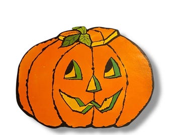 May include: A painted orange pumpkin with a carved face, ideal for Halloween decorations. The pumpkin has a green stem and leaves, with black outlines defining the features. The face includes triangular eyes and a zig-zag mouth.