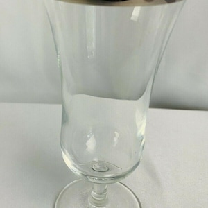 Peut inclure: Un gobelet en verre transparent avec un bord argenté. Le gobelet a une tige fine et un bol large et incurvé. Le verre est transparent. Conçu pour les boissons.