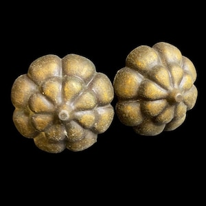 May include: Two antique brass-colored cabinet knobs with a floral design. Each knob has a rounded, textured surface with petal-like details and a central, circular indentation. The knobs are set against a black background.