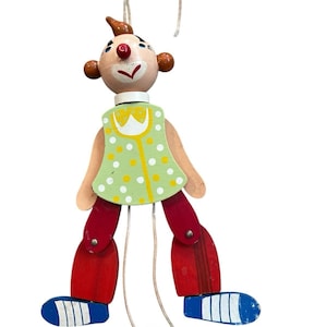 May include: A wooden pull-string puppet of a clown with a green and white polka dot shirt, red pants, and blue shoes. The puppet has a red nose, brown hair, and a white collar.