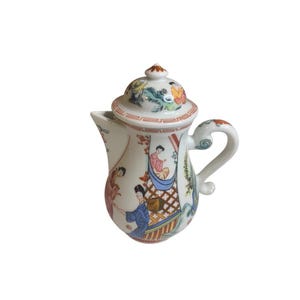 May include: A white porcelain creamer or small pitcher with a lid, featuring colorful hand-painted illustrations of figures in traditional attire, landscape elements, and a red geometric border pattern around the lid and the upper rim of the vessel.