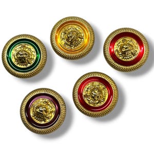May include: Five decorative buttons featuring a gold lion's head. Each button has a gold rim and a coloured enamel border in green, yellow, red, and burgundy. The buttons are round with a textured edge, suitable for clothing or crafts.
