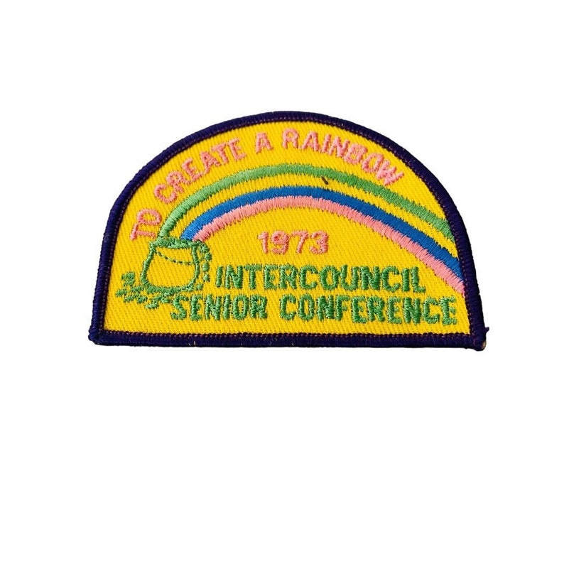 K&ouml;nnte beinhalten: Gelber Stoff-Patch mit einem Regenbogen, einem Topf voll Gold und dem Text "To Create A Rainbow 1973 Intercouncil Senior Conference".