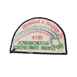 K&ouml;nnte beinhalten: Ein wei&szlig;er Stoff-Patch mit einem Regenbogen-Design und dem Text "WORK HARD & PLAY HARD" in gr&uuml;ner und rosa Schrift. Der Text "ETEI" befindet sich in der Mitte des Patches. Der Patch hat einen violetten Rand.