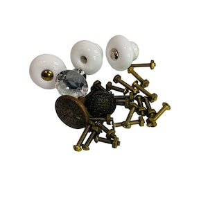May include: A collection of decorative cabinet knobs and pulls. The knobs include white ceramic, faceted crystal, and antique brass designs. The hardware also includes brass screws and bolts, suitable for furniture restoration or new projects.