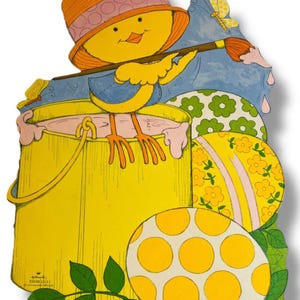 May include: A yellow chick wearing an orange hat, painting Easter eggs with a paintbrush. The chick is standing in a yellow paint bucket. The eggs are decorated with floral and polka dot patterns. The image has a Hallmark logo.