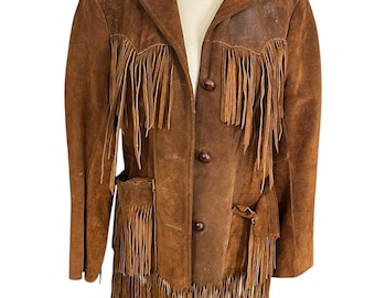 Puede incluir: Chaqueta de ante marrón con flecos en el pecho, los bolsillos y el dobladillo. La chaqueta tiene una botonadura frontal y un cuello clásico. La chaqueta se exhibe en un maniquí.