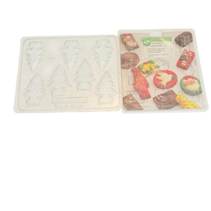 May include: Two clear plastic candy moulds. One mould features Christmas tree shapes, and the other contains various holiday-themed candy shapes, including Santa, bells, and gifts. The moulds are designed for making festive treats.