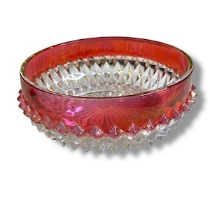 May include: A clear glass bowl with a ruby red rim and a decorative, textured exterior. The bowl's interior features a diamond-cut pattern, and the rim has a scalloped edge. The bowl is likely vintage or antique.