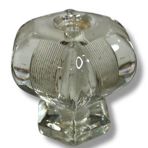 May include: Clear glass cabinet knob with a flower-like design. The knob features a rounded top with vertical ridges and a square base. The glass is transparent, allowing light to pass through, and is suitable for furniture restoration.