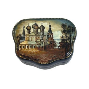 May include: A wooden box with a painted scene of a Russian church with multiple domes. The church is painted in shades of brown, gold, and white. The background is a blue sky with white clouds. The box is decorated with gold trim.