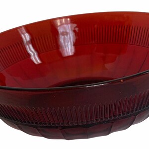 May include: A ruby red glass serving bowl with two handles. The bowl has a ribbed design around the sides and a smooth interior. The handles have a decorative, curved design. This vintage bowl is perfect for serving salads or side dishes.