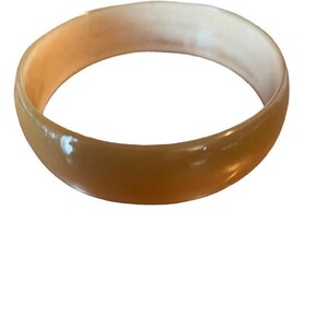 May include: A light brown bangle bracelet with a glossy finish. The bracelet is a solid, circular band, with a lighter interior color. The jewelry is set against a white background.