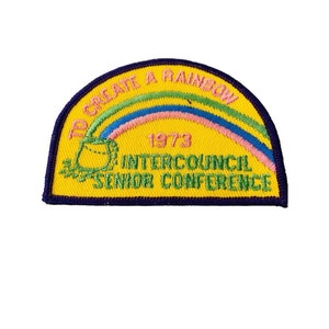 K&ouml;nnte beinhalten: Ein gelber gestickter Aufn&auml;her mit einem Regenbogen, einem Topf und dem Text "To Create A Rainbow 1973 Intercouncil Senior Conference".