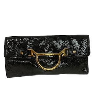 May include: Black patent leather clutch with a gold-tone ring handle and the brand name "Emanuel Ungaro" embossed on the front.