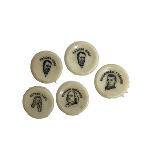 May include: Five white round bottle caps with black and white images of famous people. The caps feature images of Louis Pasteur, Isaac Newton, Benjamin Franklin, Booker T. Washington, and another image of Louis Pasteur.