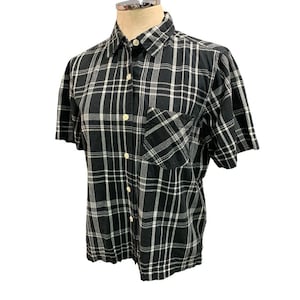 May include: A black and white checked short-sleeved shirt, buttoned up with a chest pocket. The shirt is displayed on a mannequin. The pattern is a classic design, suitable for casual wear.