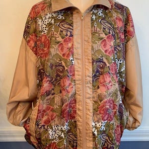 May include: A vintage floral print jacket with a tan collar, sleeves, and trim. The jacket features a full zipper and pockets. The floral pattern includes red, pink, and green flowers with paisley and animal print accents. The jacket is displayed on a mannequin.