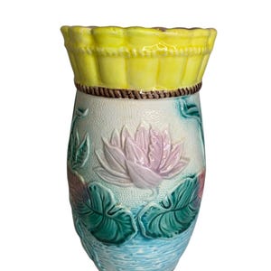 以下が含まれることがあります： 黄色い縁取りとピンクと緑の水蓮の浮き彫り模様が施された陶器の花瓶。花瓶は薄い青と白の背景になっています。