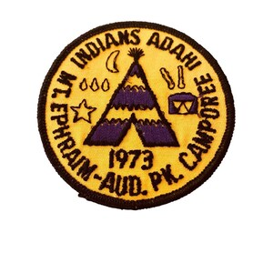 May include: Yellow round patch with black embroidered text that reads "MT. INDIANS ADAHI EPHRAIM-AUD. PK. CAMPOREE 1973". The patch features a purple and yellow teepee with a star, moon, and drums.