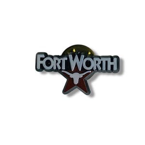 Puede incluir: Un pin con el texto "FORT WORTH" en letras blancas con un contorno negro. El pin incluye una estrella roja con una silueta de cuerno largo blanca. El pin tiene un fondo dorado.