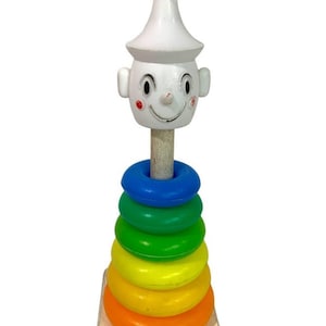 Puede incluir: Un juguete de apilar vintage Playskool con una cabeza de payaso de madera y anillos de plástico de colores. Los anillos son azules, verdes, amarillos y naranjas.