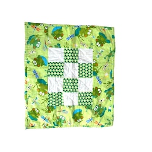 May include: A green and white patchwork quilt with a frog and dragonfly pattern. The quilt is made of squares of different fabrics, some with a green polka dot pattern and some with a white background.