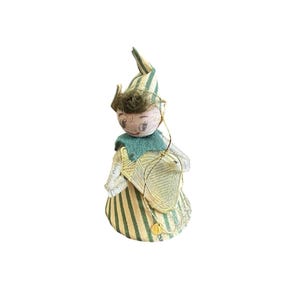 May include: A decorative figurine featuring a person with a painted face, wearing a pointed hat and a dress with green and cream vertical stripes. The figure has a green collar, white textured sleeves, and a gold-colored triangular accessory.