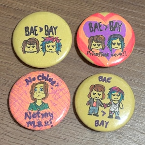 May include: Four round yellow buttons with colourful drawings and text. The buttons feature cartoon characters and the text "BAE>BAY", "Pricefield 4eva!!", "No Chloe? Not my Max", and "BAE>BAY".