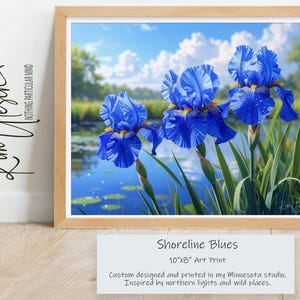 May include: A framed 10x8 inch art print titled Shoreline Blues featuring three vibrant blue iris flowers with yellow centers, dew drops on petals, and green stems. The background shows a calm blue pond, green grass, and a bright sky with white clouds.