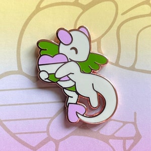 May include: A pin featuring a white cartoon dragon holding a heart with lavender and white stripes, green wings, and pink accents. The pin is set against a gradient background with the text "SHOW YOUR TRUE COLORS". The shop name "lavenderminis" is at the bottom.