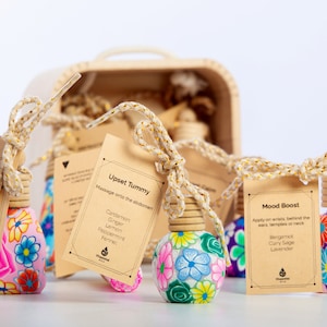 May include: Five small, colourful, floral patterned glass bottles with wooden stoppers and twine. Each bottle has a small brown card attached with text describing the scent and its uses. The scents are Sneeze Free, Upset Tummy, and Mood Boost.