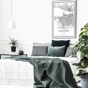 May include: A white bed with a green blanket and pillows. The bed is in a bedroom with a white wall and a black and white map of Vancouver, Canada hanging on the wall.
