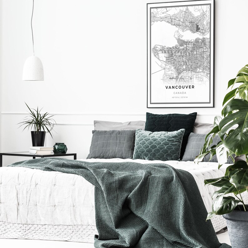 May include: A white bed with a green blanket and pillows. The bed is in a bedroom with a white wall and a black and white map of Vancouver, Canada hanging on the wall.