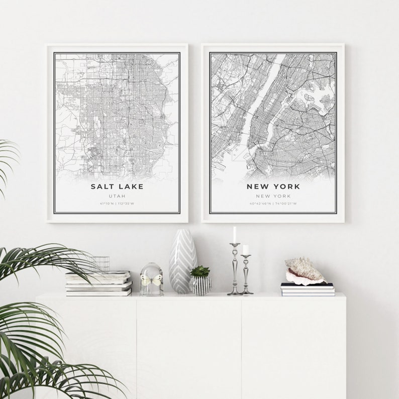 Puede incluir: Dos mapas en blanco y negro enmarcados de Salt Lake City, Utah y Nueva York, Nueva York. Los mapas est&aacute;n colgados en una pared blanca sobre un estante blanco con art&iacute;culos decorativos.