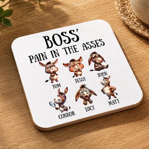 Könnte beinhalten: Ein quadratischer weißer Untersetzer mit dem schwarzen Text BOSS' PAIN IN THE ASSES über sechs Cartoon-Esel-Illustrationen. Jeder Esel ist mit einem Namen beschriftet: Tom, Jessy, John, Connor, Lucy und Matt. Die Esel zeigen verschiedene Gesichtsausdrücke.