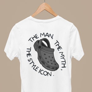 Könnte beinhalten: Weißes T-Shirt mit einer schwarzen und grauen Illustration eines Clogs auf der Rückseite. Der Text um den Clog lautet "The Man, The Myth, The Style Icon."