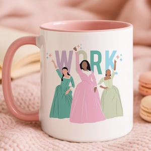 May include: White ceramic mug with a pink handle and interior. The mug features a graphic of three women in colourful dresses with the word "WORK" above them. The background is a soft pink.