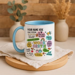 May include: White ceramic mug with a light blue interior and handle. The mug features the text "YOUR NAME HERE" and various phrases like "Work Bestie," "Partner in Crime," and "Free Therapist," along with related graphics. The mug sits on a wooden coaster.