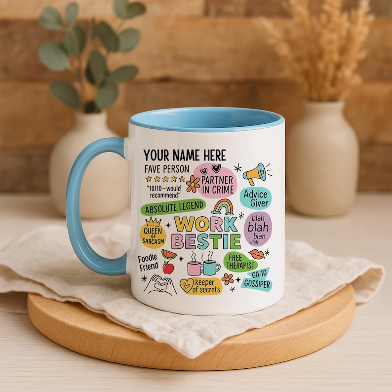 May include: White ceramic mug with a light blue interior and handle. The mug features the text "YOUR NAME HERE" and various phrases like "Work Bestie," "Partner in Crime," and "Free Therapist," along with related graphics. The mug sits on a wooden coaster.