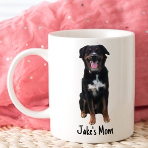 May include: White ceramic coffee mug featuring a black and white dog image and the text "Jake's Mom" printed on the front.