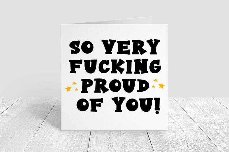 以下が含まれることがあります： 「So Very Fucking Proud Of You!」という黒い文字が書かれた白いカード。 「Proud」の両側に金色の星が2つある。