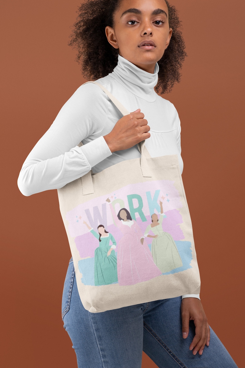 Op de afbeelding: Een witte canvas tote bag met een roze, groene en blauwe print met drie vrouwen en het woord "WORK" in grote, kleurrijke letters.
