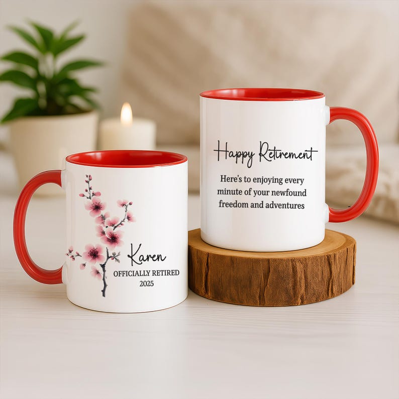May include: Two white ceramic mugs with red interiors and handles. One mug features a floral design and the text "Karen OFFICIALLY RETIRED 2025." The other mug says "Happy Retirement" with a message below. Both mugs are on a wooden surface.